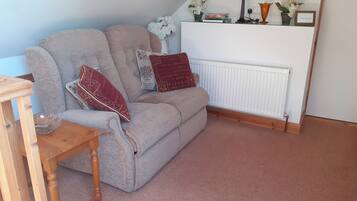 A cozy living room with a grey sofa, a wooden side table, and a radiator.