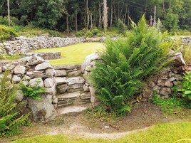 Un muro de piedra con un área de césped y helechos en un entorno natural.