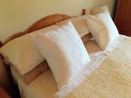 Una cama con cabecera de madera, sábanas blancas y colcha estampada.