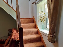 Una escalera con peldaños alfombrados, barandilla de madera y una ventana con cortina.