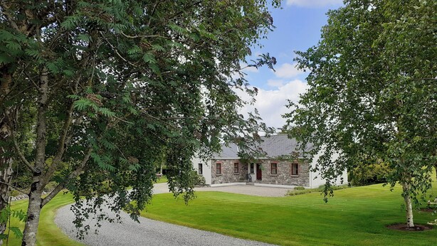 A stone house with a gravel driveway and a well-maintained lawn. - Fraoch Cottage (Garrykennedy)