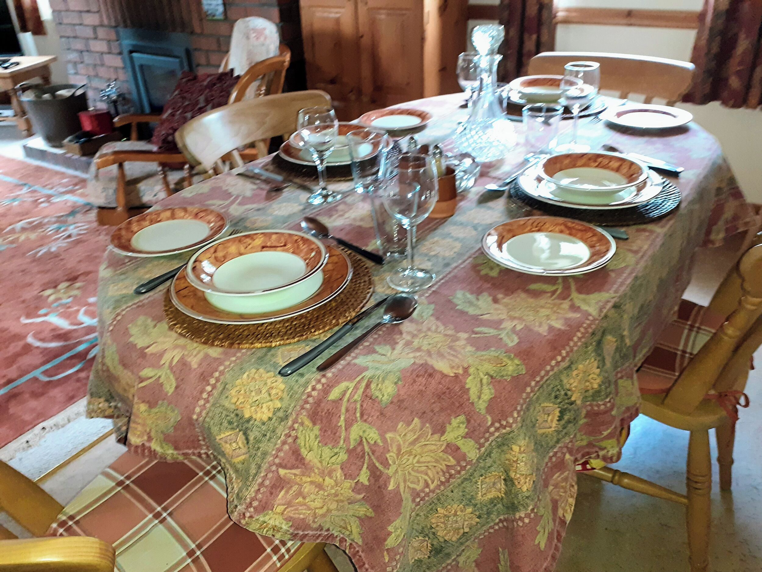 Una mesa de comedor lista con platos, tazones, cubiertos y vasos, cubierta por un mantel estampado.