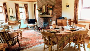 A dining area with a brick fireplace, wooden furniture, and a table set for a meal. - Fraoch Cottage (Garrykennedy)