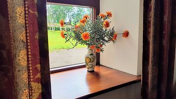 Een raam met een houten vensterbank, een vaas met oranje bloemen en uitzicht op een groen landschap.
