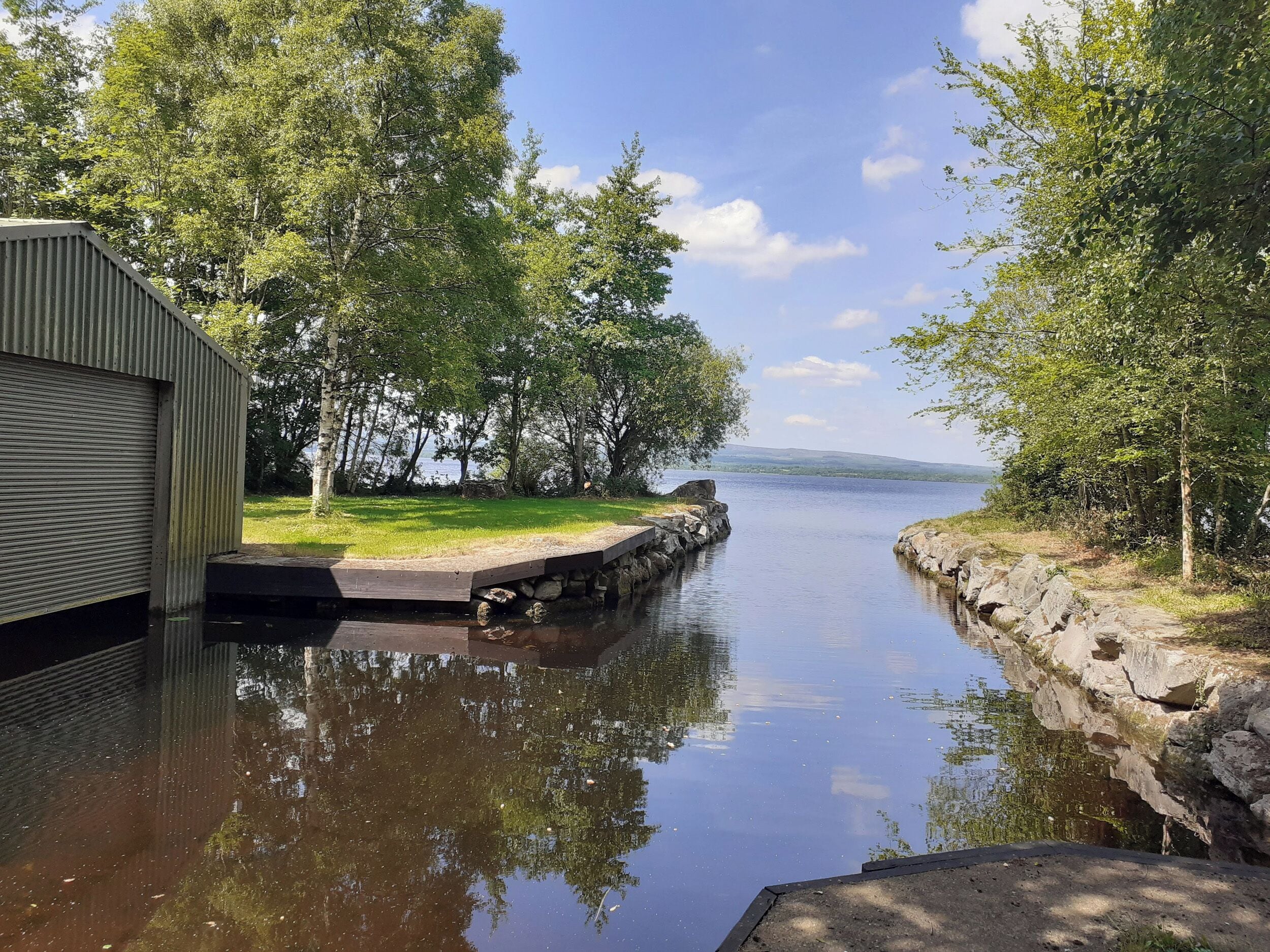 A calm water body with a wooden dock, surrounded by trees and a grassy area.