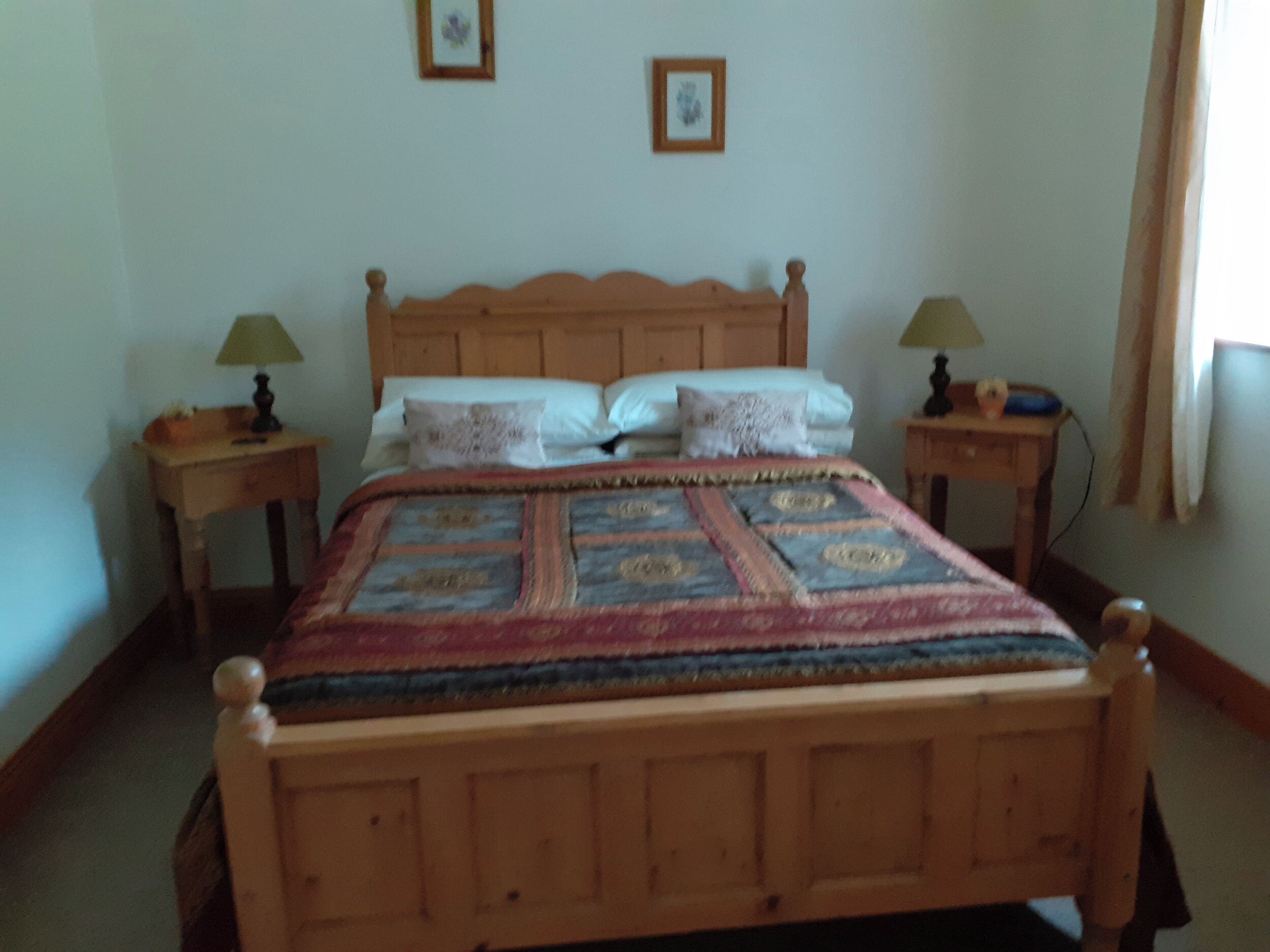 Un lit en bois surmonté d’une couvre-lit à motifs, deux tables de chevet avec des lampes et deux tableaux encadrés accrochés au mur.