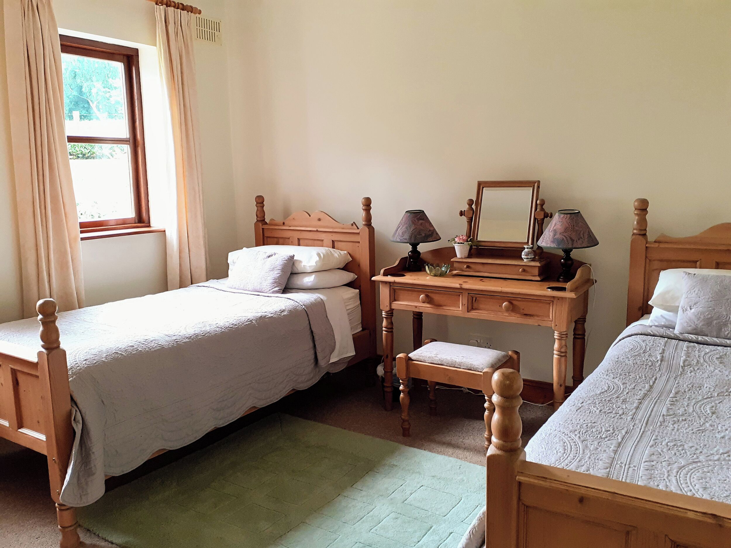 A bedroom with two single beds, a wooden dresser, a mirror, and a window with curtains.