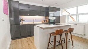 Eine moderne Küche mit dunklen Schränken, einer zentralen Kochinsel mit Barhocker und einem großen Fenster für natürliches Licht.
