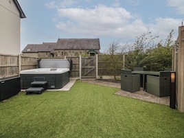 Un patio trasero con jacuzzi, mobiliario exterior y una valla de madera.