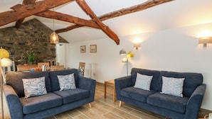 A cozy living room with two blue sofas, a stone wall, wooden beams, and a tiled floor.