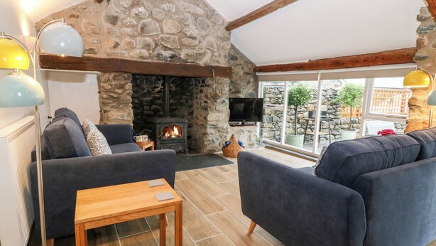 A cozy living room with a stone fireplace, comfortable seating, and a large window offering a view of the outdoors.