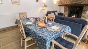 A cozy dining area with a table set for two, a stone fireplace, and a blue sofa in the background.