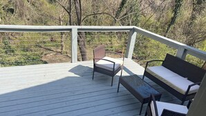 Eine Holzterrasse mit weißer Reling, zwei Korbstühle und eine Bank.