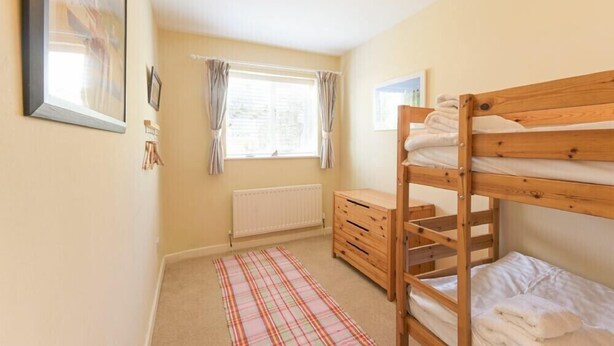 Quarto com uma cama beliche, cômoda de madeira, radiador e janela com cortinas.
