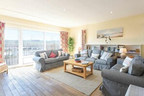 A spacious living room with two grey sofas, a wooden coffee table, and a bookshelf.