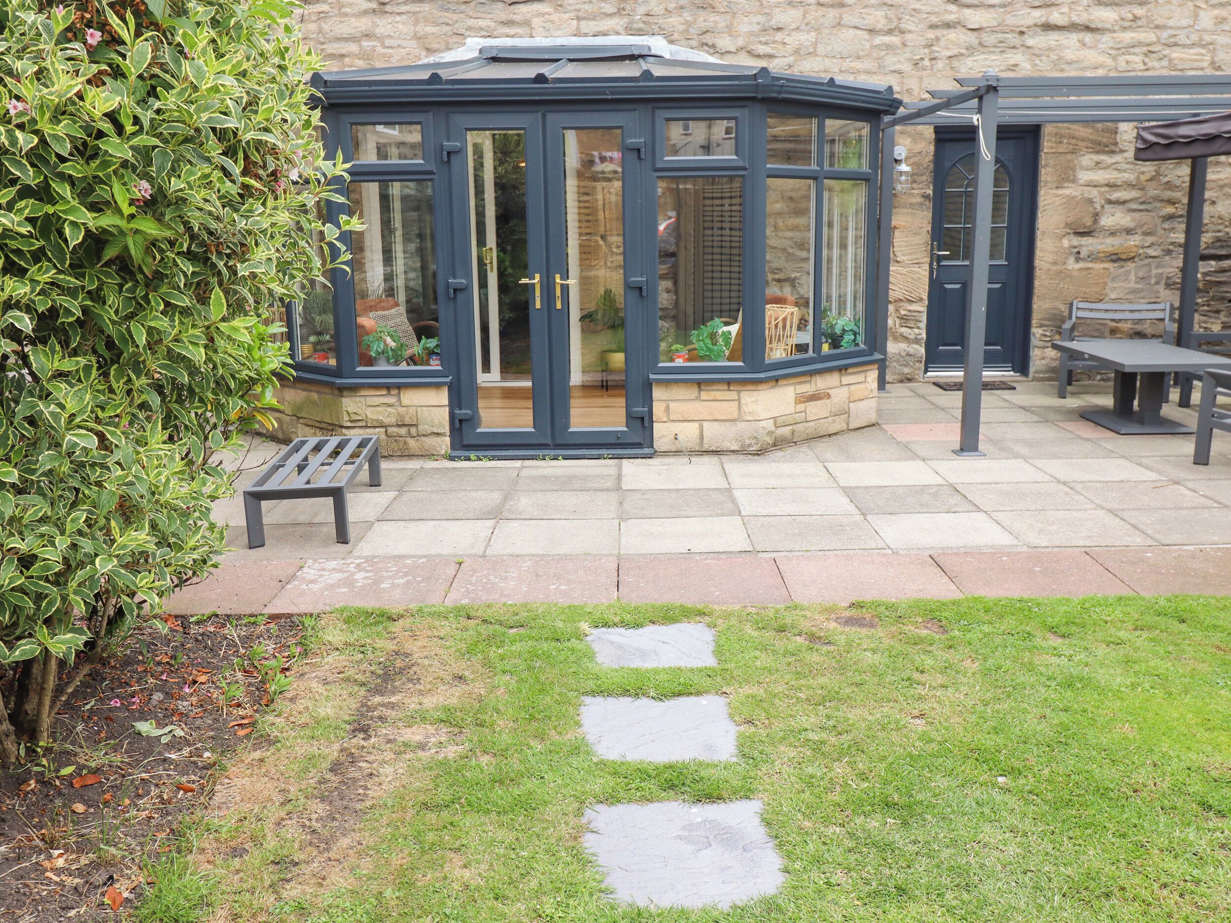 A conservatory with a stone base, a bench, and a stone pathway leading to it.