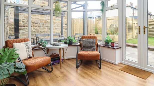 A conservatory with a stone wall, two leather chairs, a small table, and potted plants.