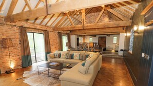 A spacious living room with a herringbone wooden floor, a large beige sofa, and a herringbone wooden ceiling. - The Stables (Ledbury)