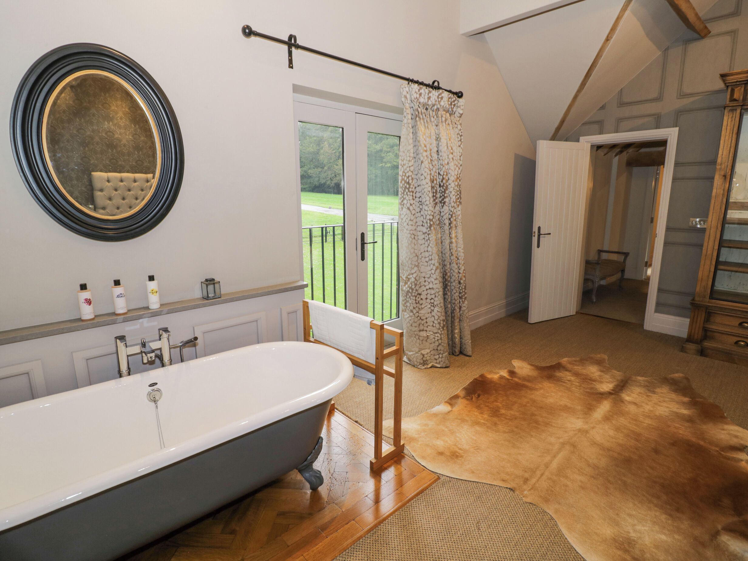 A bathroom with a freestanding bathtub, a large mirror, and a view of a balcony with a door leading to another room.