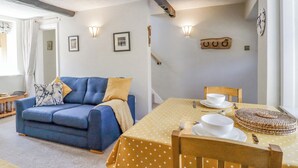 A cozy living room with a blue sofa, a dining table set with plates and a bowl, and a wall-mounted clock. - Hawthorn (Keighley)