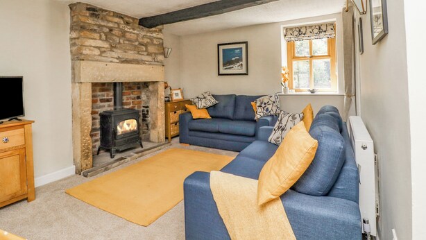 A living room with a stone fireplace, a blue sofa, and a wooden cabinet. - Hawthorn (Keighley)