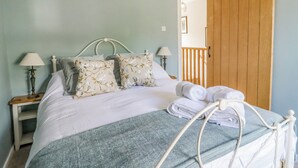 A neatly made bed with floral pillows, a blue blanket, and a wooden door in the background. - Hawthorn (Keighley)