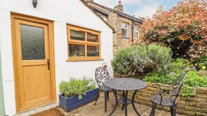 A quaint cottage with a wooden door, a window, and a small patio with a table and chairs. - Hawthorn (Keighley)