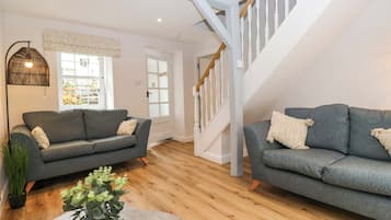 A spacious living room with two grey sofas, a wooden floor, a staircase, and a large window with a view.