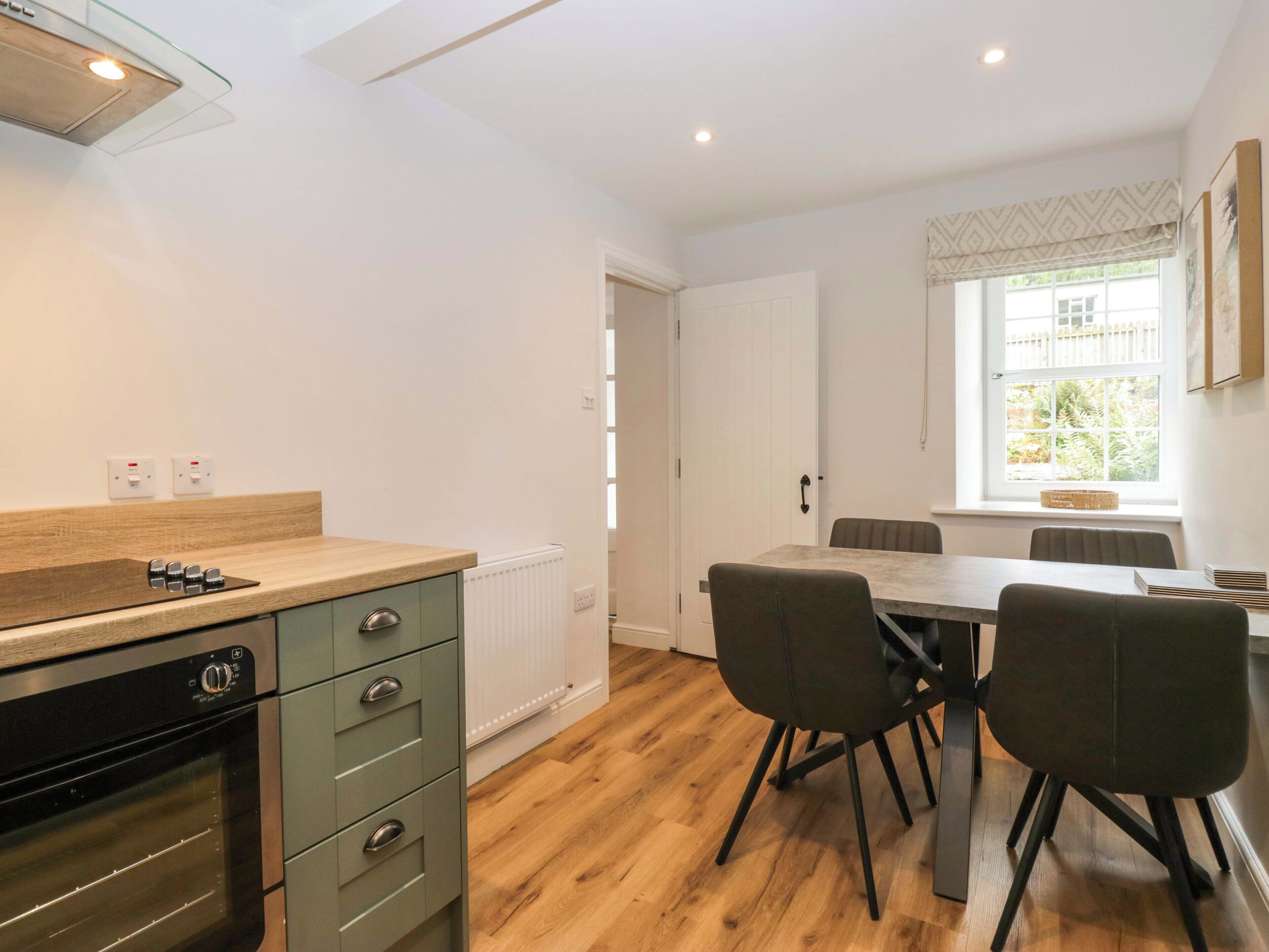 A modern kitchen with a built-in oven, a dining area with a table and chairs, and a window with a view of greenery.