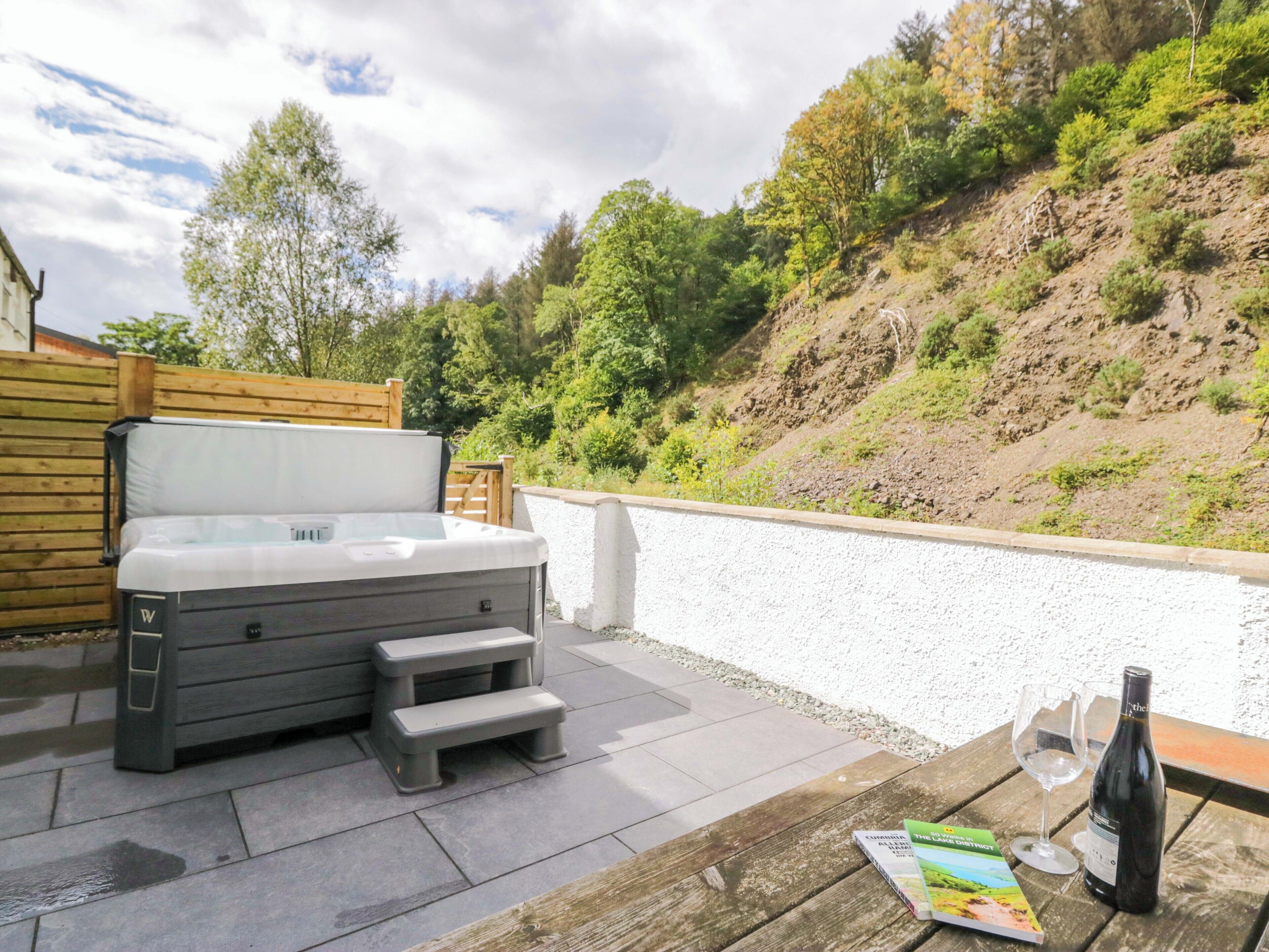A hot tub with steps, a wooden table with a bottle of wine and a glass, and a magazine on the table.