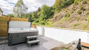 A hot tub with steps, a wooden table with a bottle of wine and a glass, and a magazine on the table.