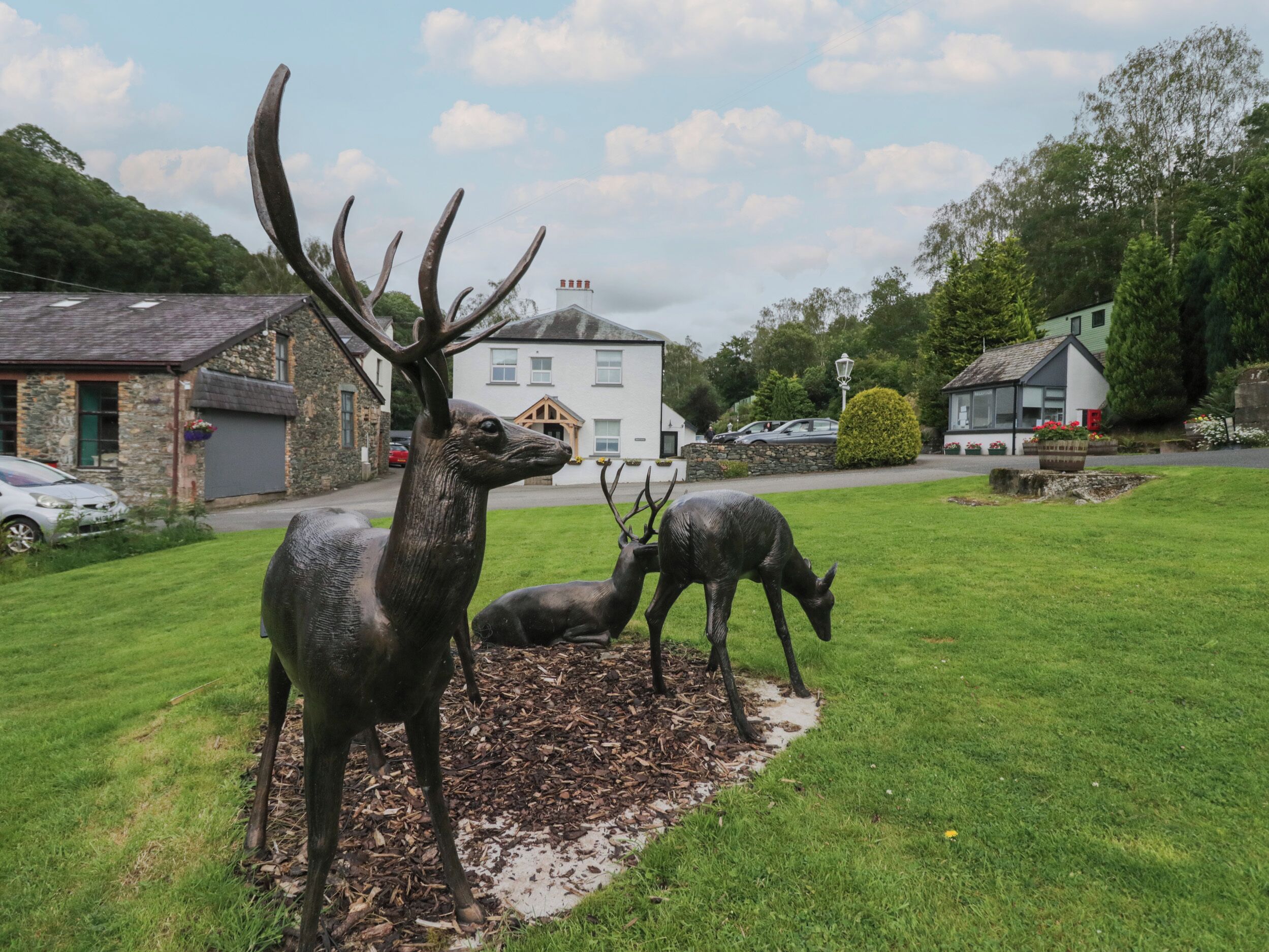 A grassy area with deer statues and a stone building in the background.