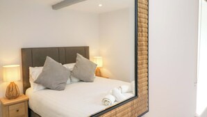 A neatly made bed with pillows, a bedside lamp, and a large mirror reflecting the room. - Riverside Cottage No 4 (Keswick)