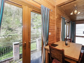 Un intérieur en bois comprenant une table à manger, des chaises, des rideaux et une vue sur un paysage naturel grâce à de grandes fenêtres.