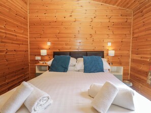 A wooden-paneled room with a bed, two bedside tables, and two lamps. - Elm Lodge (Keswick)