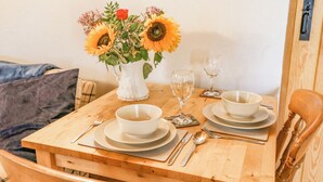 A wooden dining table with a white vase of sunflowers and a red rose, two white bowls, and a set of cutlery. - Ty Bach Twt (Llandysul)