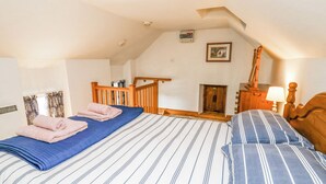 A bedroom with a sloped ceiling, a wooden bed frame, a small fireplace, and a wooden staircase. - Ty Bach Twt (Llandysul)