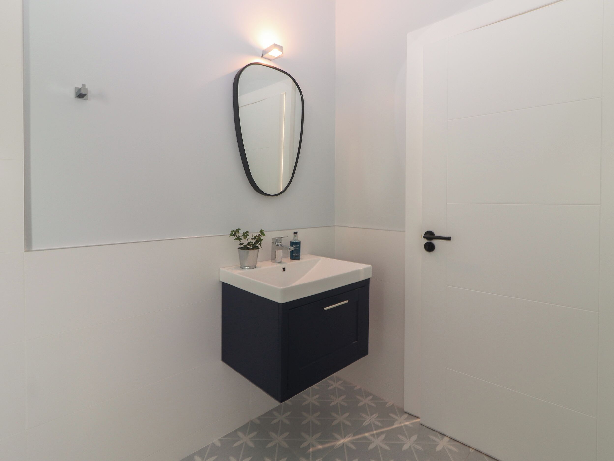 A bathroom with a white sink, dark cabinet, and a mirror with a light above it.