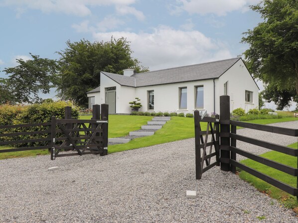 A white house with a grey roof, a gravel driveway, and a wooden fence. - Shannon Vale (Woodford)