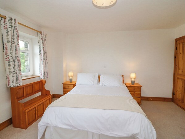 A bedroom with a bed, two bedside tables with lamps, a wooden bench, and a window with curtains. - Coorlacka (Goleen)