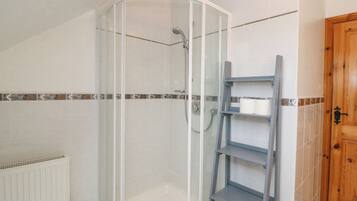Un baño con cabina de ducha de vidrio, un radiador blanco y una puerta de madera.