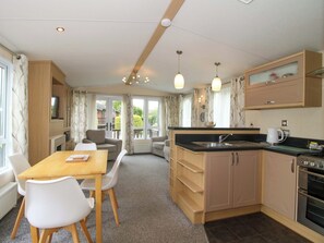 A compact kitchen with a dining area, wooden cabinets, a built-in oven, and a view to the outside. - Dove (Leominster)