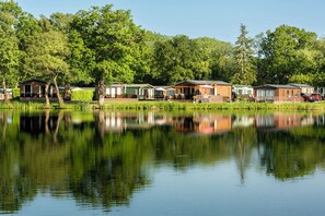 A row of cabins by a calm lake with reflections, surrounded by lush greenery. - Dove (Leominster)