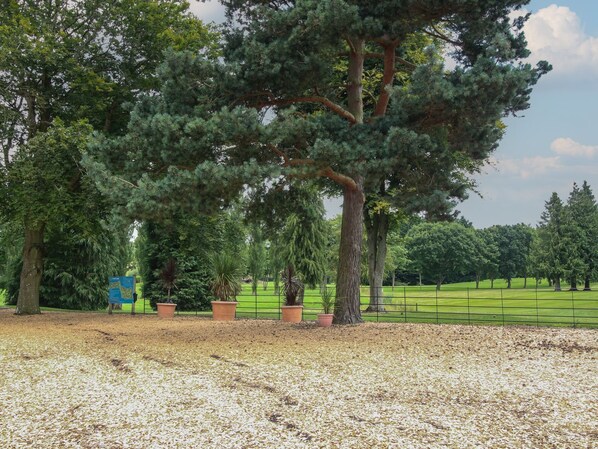 Un parque con un árbol grande, un cartel con mapa y una zona cubierta de césped y hojas dispersas.