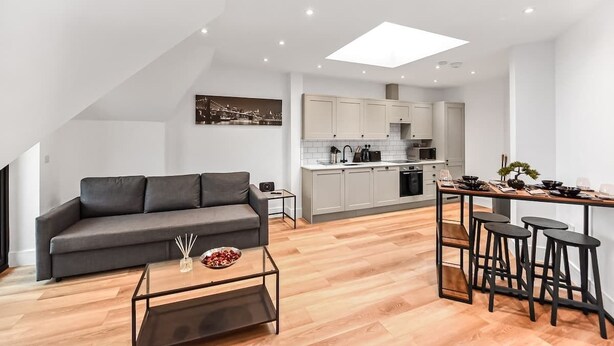 A modern apartment with a living area, kitchenette, and a dining space with stools. - Stylish East Croydon Apartment w/ Balcony & Fast WiFi (Greater London)