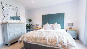 A modern bedroom with a grey bed, a teal headboard, and a decorative mirror on the wall. - Briery House (Keswick)