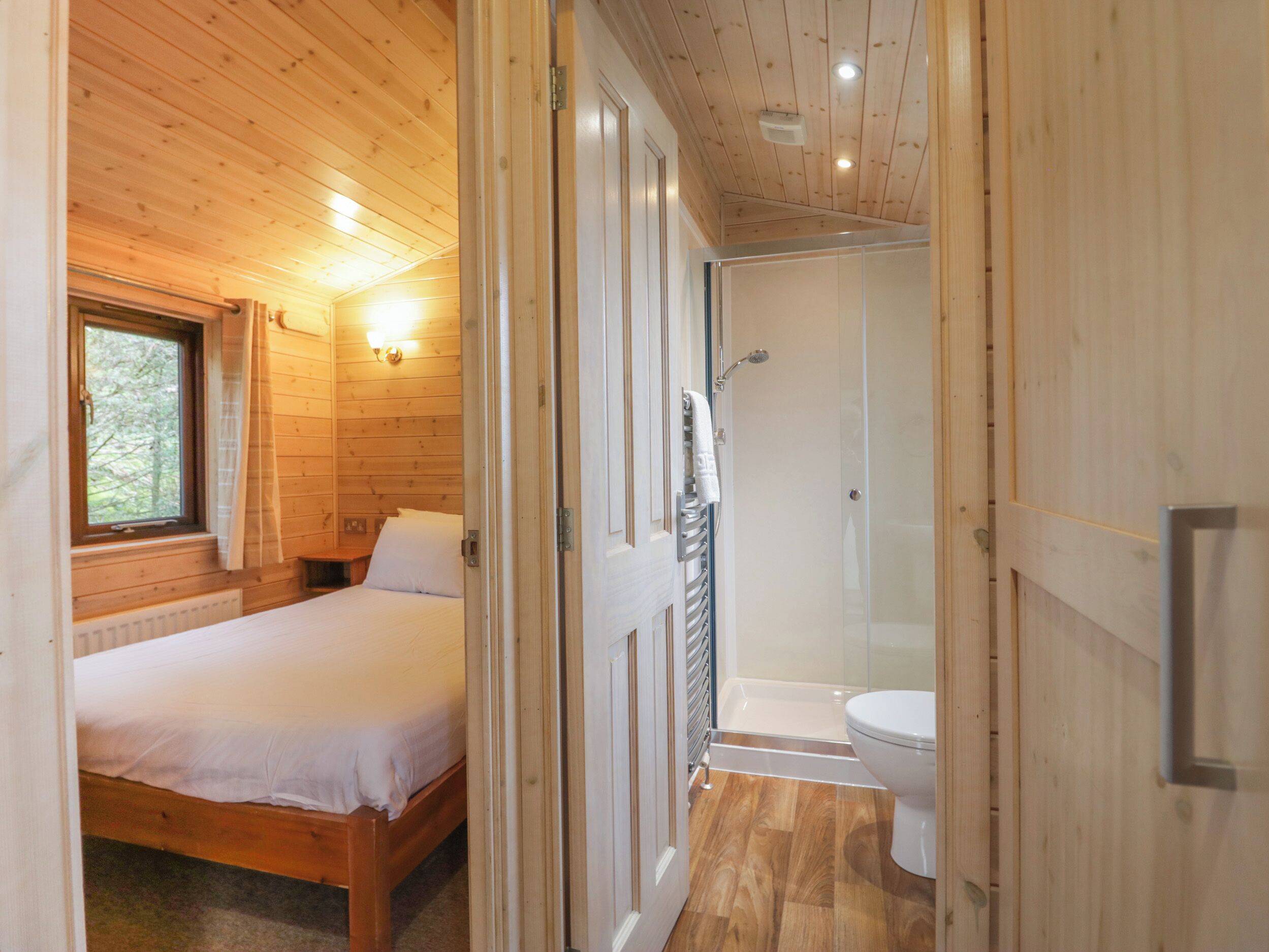 Quarto de cabana de madeira com uma cama, uma janela e um banheiro com chuveiro e vaso sanitário.