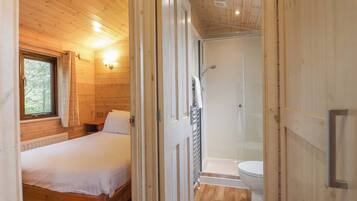Quarto de cabana de madeira com uma cama, uma janela e um banheiro com chuveiro e vaso sanitário.