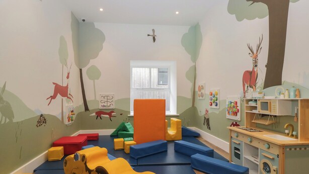 Ein Kinderspielzimmer mit Spielmatte, Schaumstoffbausteinen und einer Spielküche.