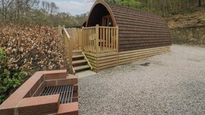A wooden cabin with a sloped roof, a wooden porch, and a gravel driveway. - Pod No 6 (Keswick)
